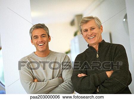 Stock Photograph - Men standing next to each other crossing arms, laughing, portrait.. Fotosearch