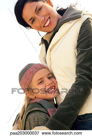 Young woman cocking head, waist up, little girl leaning against her, smiling View Large Photo Image Stock Photo - Young woman cocking head, waist up, little girl leaning against her, smiling. Fotosearch