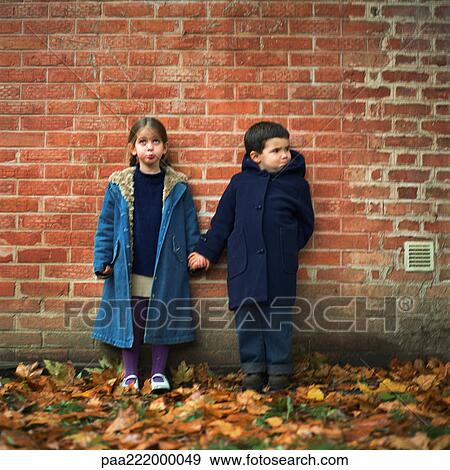 Boy and girl holding hands and making faces in front of brick wall, full length View Large Photo Image Stock Photo - Boy and girl holding hands and making faces in front of brick wall, full length. Fotosearch