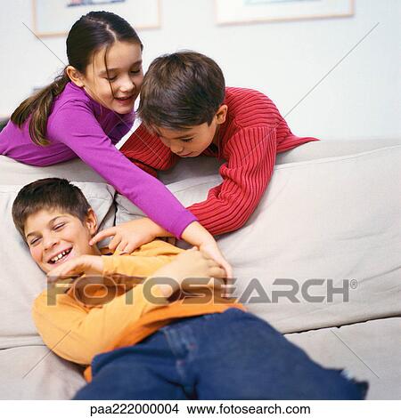 Boy and girl leaning over sofa, tickling second boy on sofa View Large Photo Image Picture - Boy and girl leaning over sofa, tickling second boy on sofa. Fotosearch
