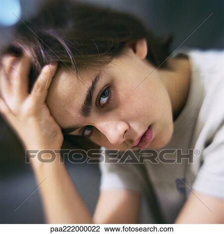 Stock Image - Boy holding head, looking at camera, close-up. Fotosearch