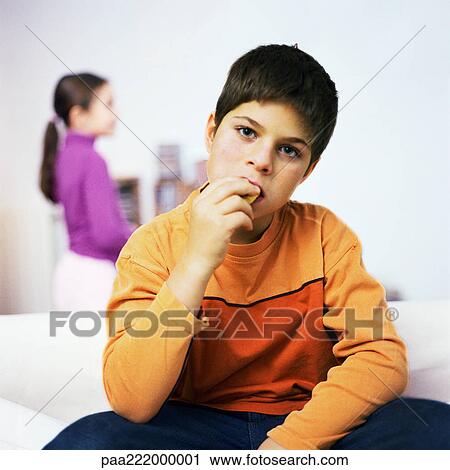 Boy sitting on sofa, eating, girl standing in background View Large Photo Image Stock Image - Boy sitting on sofa, eating, girl standing in background. Fotosearch