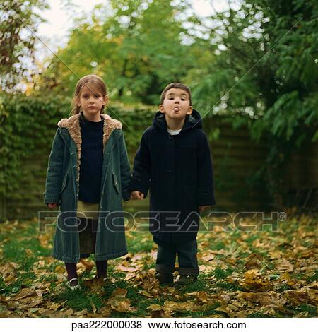 Stock Photo - Girl and boy holding hands outside, boy sticking out tongue. Fotosearch