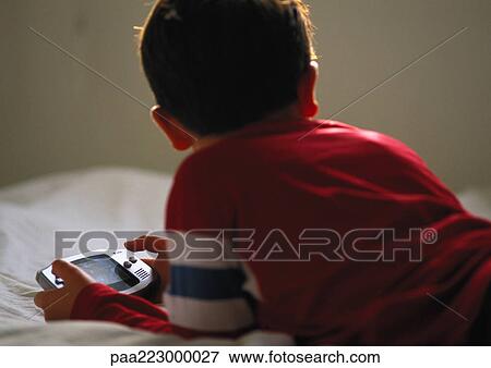 Young boy lying on bed playing video game. View Large Photo Image Stock Photo - Young boy lying on bed playing video game.. Fotosearch
