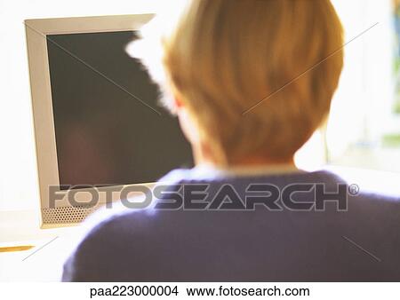 Young boy sitting at computer monitor, rear view View Large Photo Image Picture - Young boy sitting at computer monitor, rear view. Fotosearch