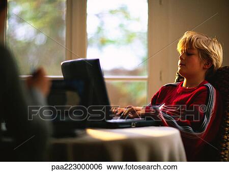 Young boy sitting at table using computer, second person blurred in foreground View Large Photo Image Stock Photograph - Young boy sitting at table using computer, second person blurred in foreground. Fotosearch