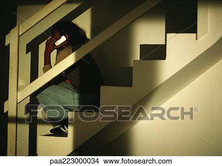 Picture - Young boy sitting on stairs talking on phone.. Fotosearch