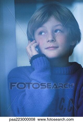 Stock Photo - Young boy talking on phone, looking out window, portrait. Fotosearch