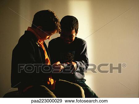 Young boys sitting and looking at video game. View Large Photo Image Stock Photo - Young boys sitting and looking at video game.. Fotosearch