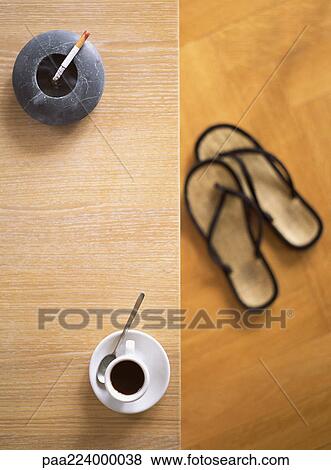 Ashtray with cigarette and cup of coffee on table, flipflops on floor, high angle view View Large Photo Image Stock Photo - Ashtray with cigarette and cup of coffee on table, flipflops on floor, high angle view. Fotosearch