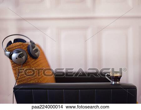 Headphones resting on chair back, cup sitting on chair arm. View Large Photo Image Picture - Headphones resting on chair back, cup sitting on chair arm.. Fotosearch