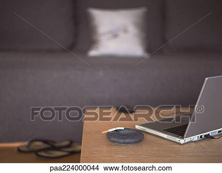 Laptop on table next to ashtray, sofa in background View Large Photo Image Picture - Laptop on table next to ashtray, sofa in background. Fotosearch