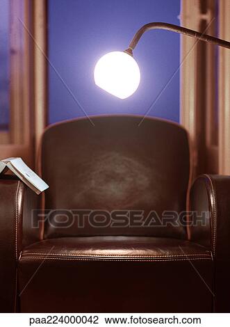 Stock Image - Light shining over chair with open book on arm. Fotosearch