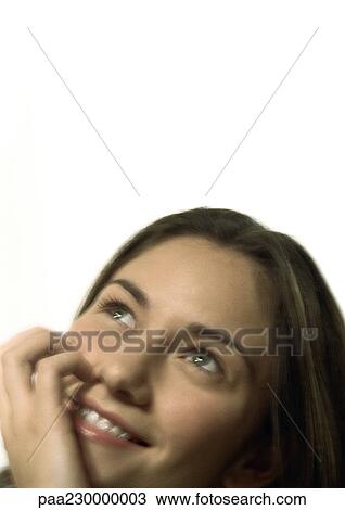 Stock Image - Woman looking up, smiling, hand on face, portrait.. Fotosearch