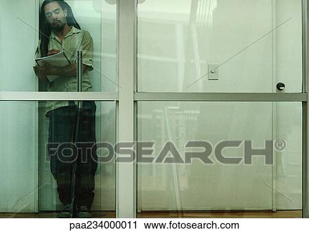 Man leaning against wall reading, view through glass. View Large Photo Image Stock Image - Man leaning against wall reading, view through glass.. Fotosearch