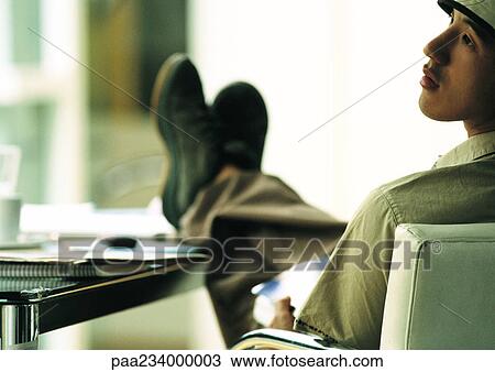 Man sitting in chair with feet on table, looking to the side, rear view. View Large Photo Image Stock Image - Man sitting in chair with feet on table, looking to the side, rear view.. Fotosearch