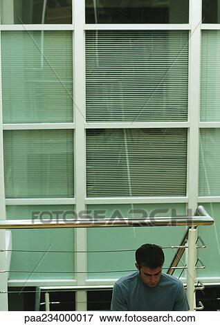 Man sitting, leaning against metal rails, window in background View Large Photo Image Stock Photo - Man sitting, leaning against metal rails, window in background. Fotosearch