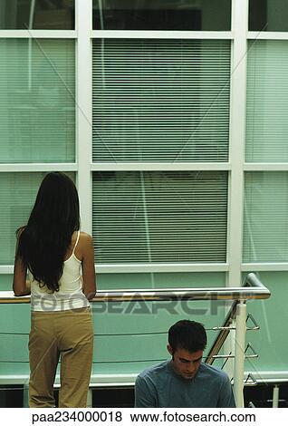 Man sitting, leaning against metal rails, and woman standing next to him, rear view View Large Photo Image Stock Photo - Man sitting, leaning against metal rails, and woman standing next to him, rear view. Fotosearch
