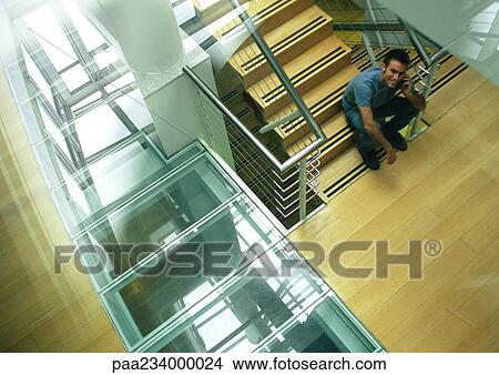 Man sitting on stairs talking on cell phone looking up, view from above. View Large Photo Image Picture - Man sitting on stairs talking on cell phone looking up, view from above.. Fotosearch