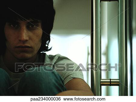 Stock Photograph - Man sitting with knees up, looking at camera, close up.. Fotosearch