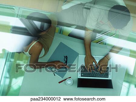 Man working on laptop, woman sitting on table pointing at laptop, through glass, high angle view. View Large Photo Image Stock Image - Man working on laptop, woman sitting on table pointing at laptop, through glass, high angle view.. Fotosearch