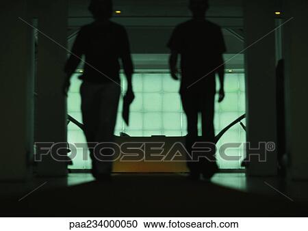 Stock Image - Two people walking through doorway of office, silhouette.. Fotosearch