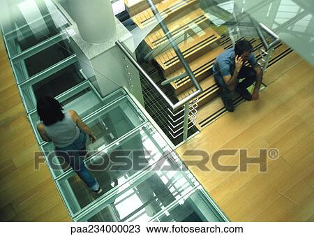 Woman walking past man sitting on stairs talking on cell phone, view from above. View Large Photo Image Stock Image - Woman walking past man sitting on stairs talking on cell phone, view from above.. Fotosearch