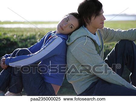 Stock Photography - Man and woman sitting back to back by water.. Fotosearch