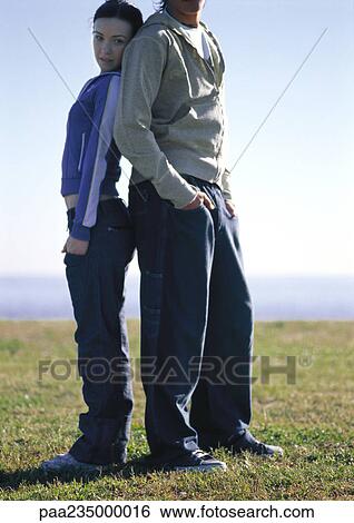 Man and woman standing back to back on grass by the water. View Large Photo Image Stock Photograph - Man and woman standing back to back on grass by the water.. Fotosearch