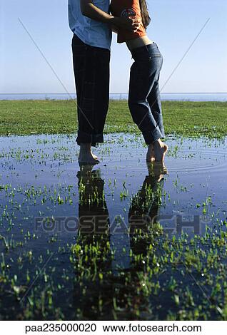 Man and woman standing in a puddle on grass by water. View Large Photo Image Stock Image - Man and woman standing in a puddle on grass by water.. Fotosearch