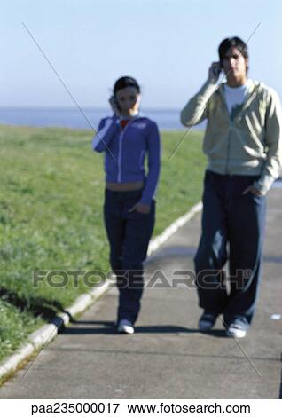 Stock Photo - Man and woman with cell phones walking on sidewalk.. Fotosearch
