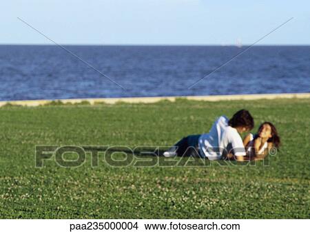 Picture - Man and women laying together on grass by water, blurred.. Fotosearch