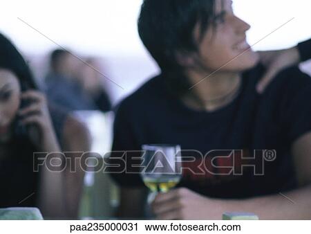 Stock Image - Man drinking wine sitting next to woman on cell phone.. Fotosearch