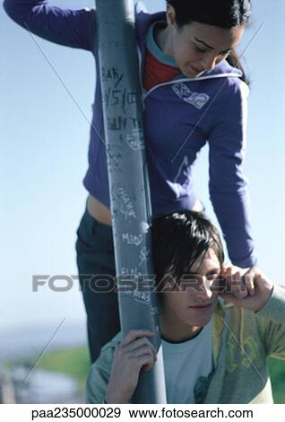 Stock Photo - Man on phone holding onto pole, talking on cell phone with woman standing above him.. Fotosearch