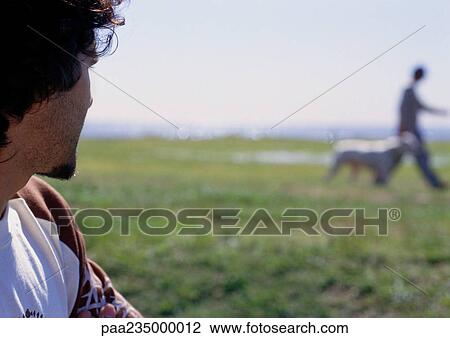 Man sitting looking at man walking dog by water. View Large Photo Image Stock Image - Man sitting looking at man walking dog by water.. Fotosearch