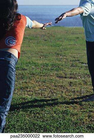 Stock Image - Young man and woman reaching their hands out to each other.. Fotosearch
