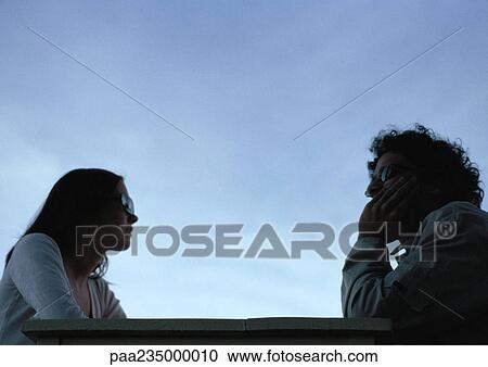 Young man and young woman sitting at table with sky in background. View Large Photo Image Stock Image - Young man and young woman sitting at table with sky in background.. Fotosearch