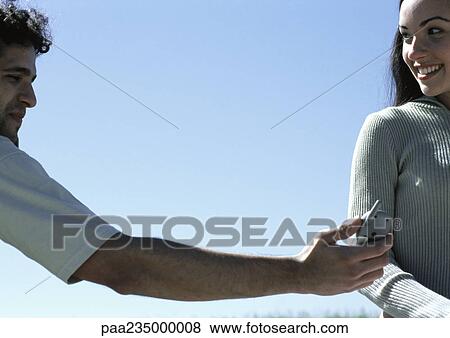 Young man handing cell phone to young woman with sky in background. View Large Photo Image Stock Photo - Young man handing cell phone to young woman with sky in background.. Fotosearch