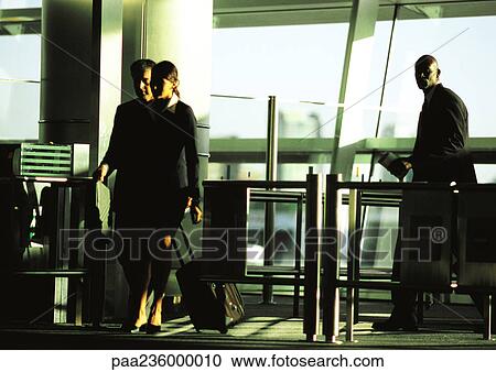 Stock Image - Businessman and businesswoman walking through security gate with suitcases. Fotosearch