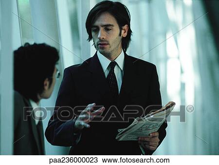 Businessman holding newspaper, gesturing and talking to second businessman View Large Photo Image Stock Image - Businessman holding newspaper, gesturing and talking to second businessman. Fotosearch