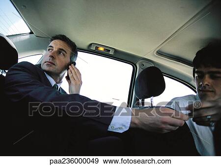 Businessman on cell phone in backseat of car paying taxi driver, low angle view View Large Photo Image Stock Photo - Businessman on cell phone in backseat of car paying taxi driver, low angle view. Fotosearch