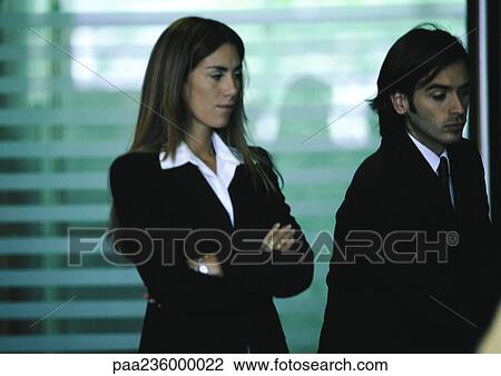Stock Image - Businessman standing next to businesswoman with arms crossed.. Fotosearch