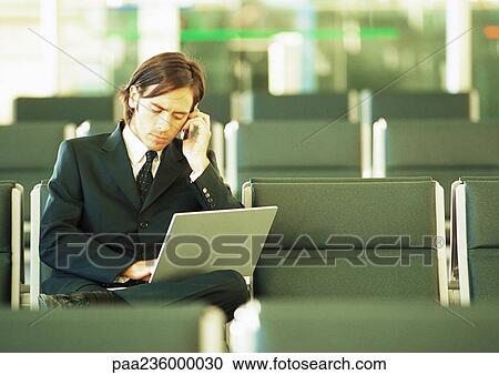 Businessman using cell phone and working on laptop in airport lounge View Large Photo Image Stock Image - Businessman using cell phone and working on laptop in airport lounge. Fotosearch