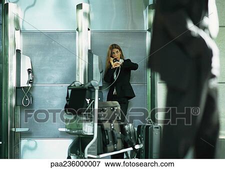 Stock Photo - Businesswoman talking on public pay phone in airport. Fotosearch