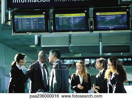 Group of businesspeople standing together, talking under airport departure and arrival monitors. View Large Photo Image Stock Photograph - Group of businesspeople standing together, talking under airport departure and arrival monitors.. Fotosearch