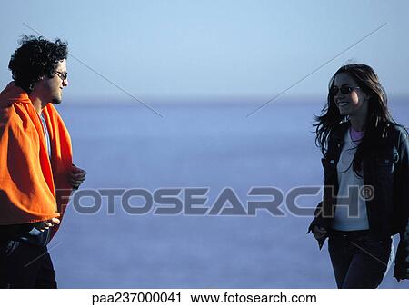 Man with orange blanket around shoulders looking at woman near water. View Large Photo Image Stock Image - Man with orange blanket around shoulders looking at woman near water.. Fotosearch