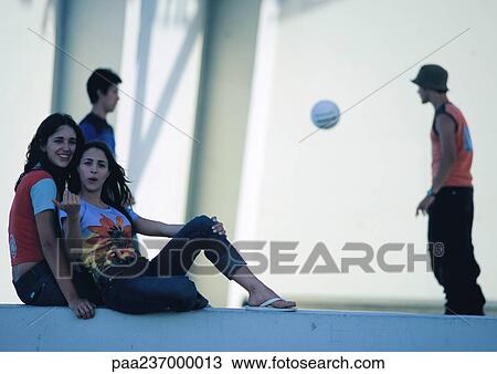 Two women sitting, one gesturing with hand, two men playing soccer in background. View Large Photo Image Stock Image - Two women sitting, one gesturing with hand, two men playing soccer in background.. Fotosearch