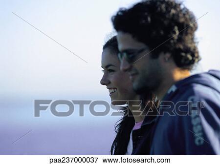 Young man standing next to young woman, smiling, side view View Large Photo Image Stock Photo - Young man standing next to young woman, smiling, side view. Fotosearch