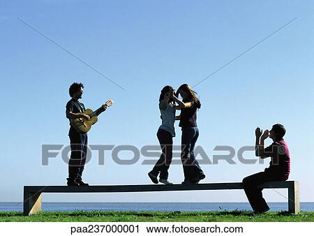 Stock Image - Young people playing on bench near water. Fotosearch