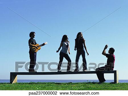 Stock Image - Young people playing on bench near water. Fotosearch